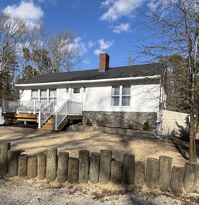 back of property with roof with shingles, a chimney, fence, stone siding, and a wooden deck