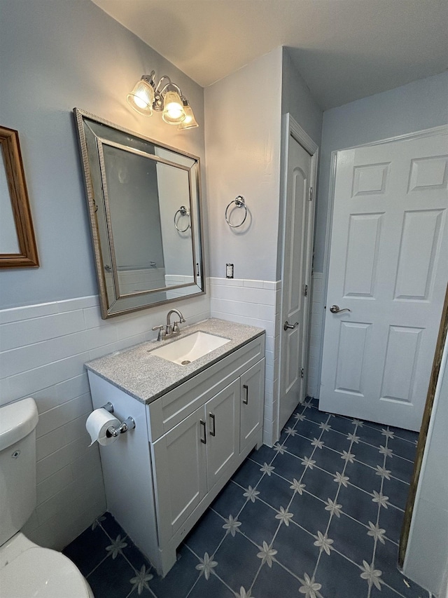 bathroom with toilet, a wainscoted wall, tile walls, and vanity