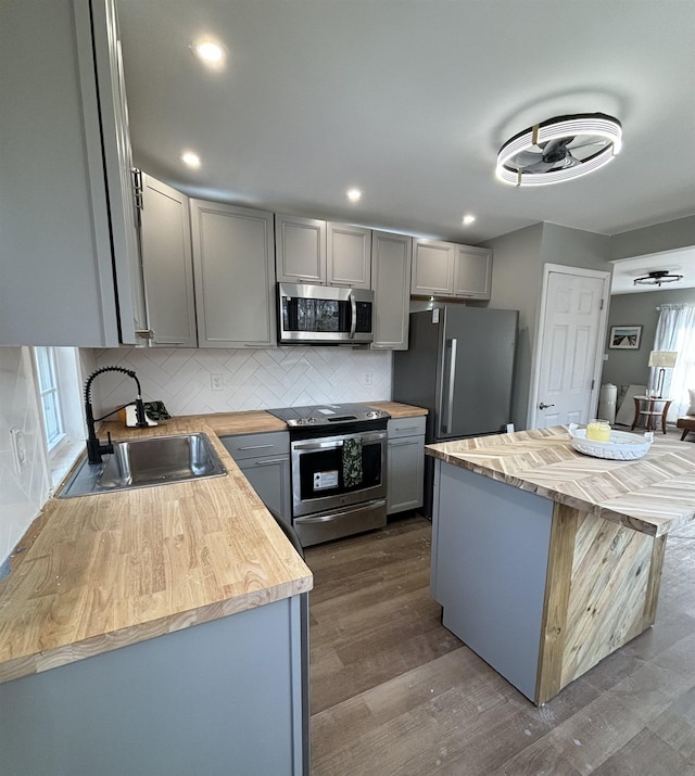 kitchen with butcher block countertops, appliances with stainless steel finishes, a sink, and gray cabinetry