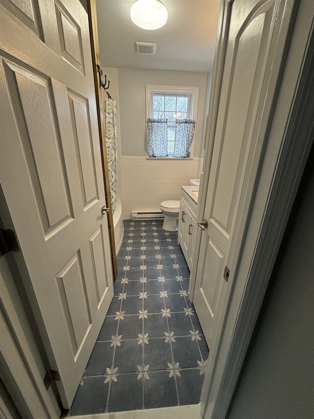 bathroom with a wainscoted wall, visible vents, baseboard heating, toilet, and vanity