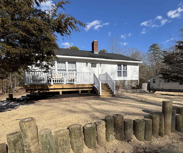 rear view of property with a shingled roof, a chimney, and a deck