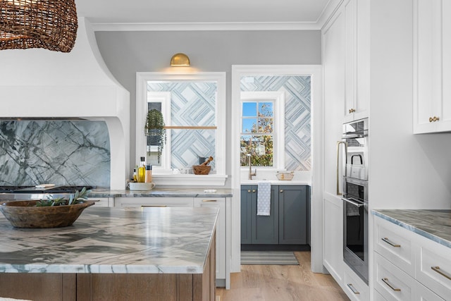 kitchen featuring white cabinetry, crown molding, oven, and light stone countertops