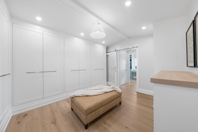 walk in closet featuring light wood-type flooring, lofted ceiling with beams, and a barn door