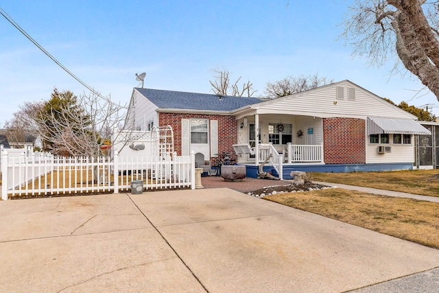 view of front of property with a porch, brick siding, fence, driveway, and roof with shingles