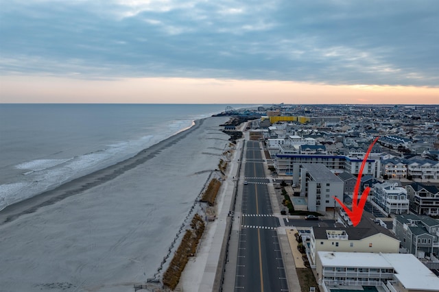 aerial view at dusk featuring a water view and a beach view