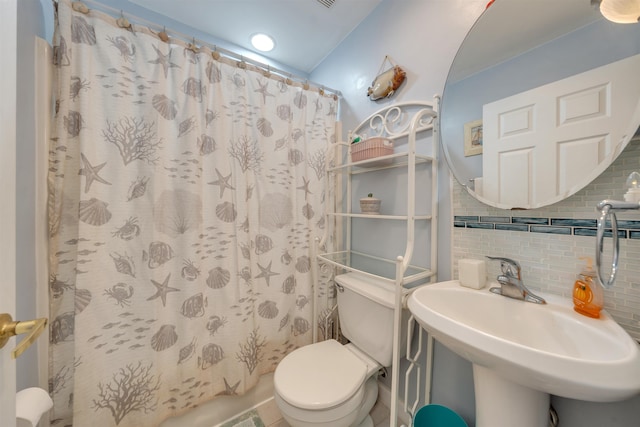 bathroom featuring curtained shower, a sink, toilet, and decorative backsplash