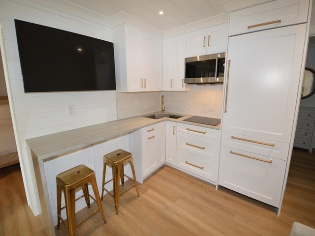177 80th St Unit 104, Avalon, NJ 08202 - kitchen with stainless steel microwave, a sink, black electric stovetop, light wood-style flooring, and white cabinetry