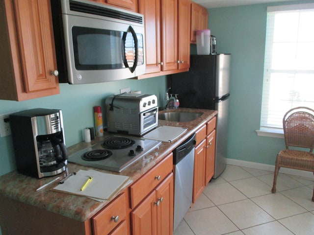 kitchen with light tile patterned floors, stainless steel appliances, brown cabinets, and a sink