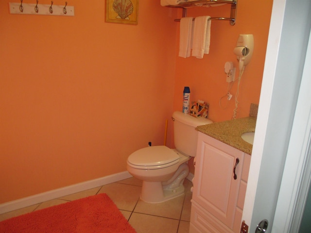 half bathroom with vanity, tile patterned floors, toilet, and baseboards