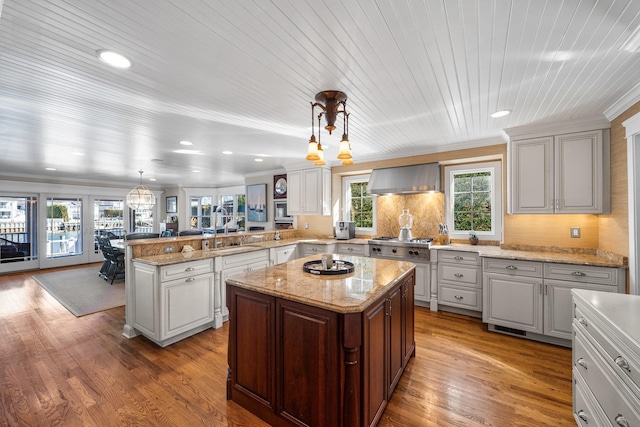 kitchen with a peninsula, wall chimney exhaust hood, light wood-style floors, and a sink