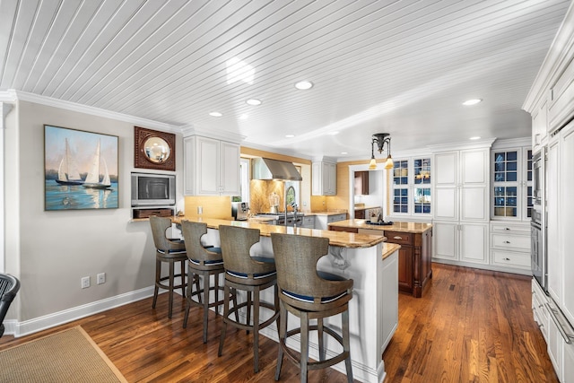 kitchen with glass insert cabinets, a breakfast bar, a peninsula, wall chimney exhaust hood, and dark wood-style flooring