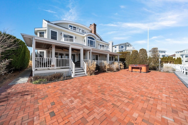 shingle-style home with a hot tub, ceiling fan, a porch, a chimney, and a balcony