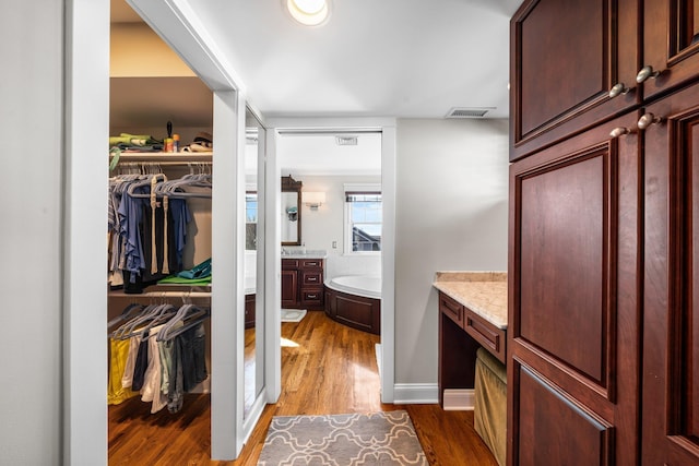 bathroom featuring vanity, wood finished floors, visible vents, a walk in closet, and a bath