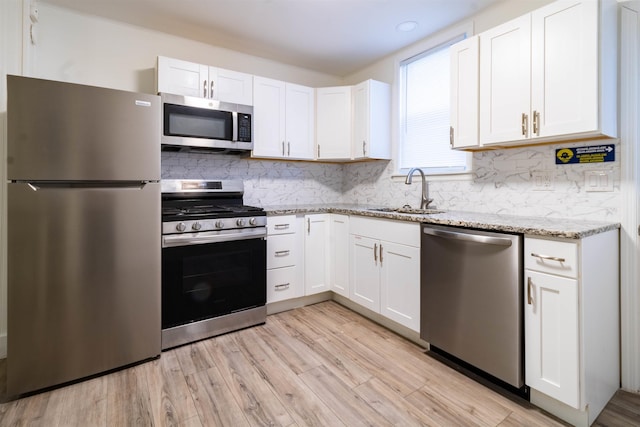 kitchen featuring sink, white cabinetry, backsplash, stainless steel appliances, and light stone countertops