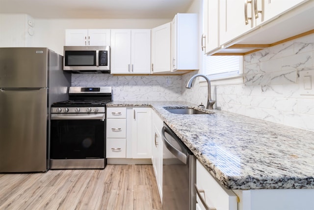 kitchen with sink, light hardwood / wood-style flooring, appliances with stainless steel finishes, light stone counters, and white cabinets