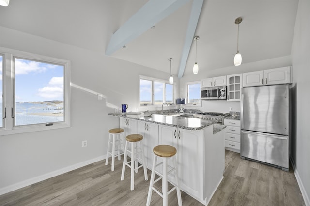 kitchen with kitchen peninsula, stainless steel appliances, pendant lighting, lofted ceiling with beams, and white cabinetry