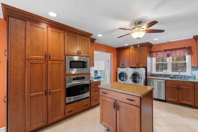 kitchen with brown cabinetry, light stone counters, stainless steel appliances, washer and dryer, and a sink