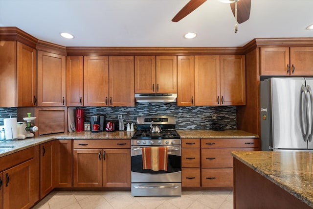 kitchen featuring brown cabinets, under cabinet range hood, stainless steel appliances, and dark stone countertops