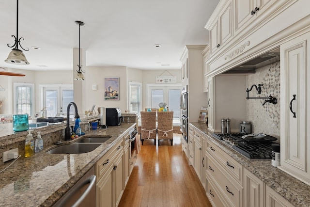 kitchen featuring custom exhaust hood, sink, hanging light fixtures, light wood-type flooring, and light stone counters