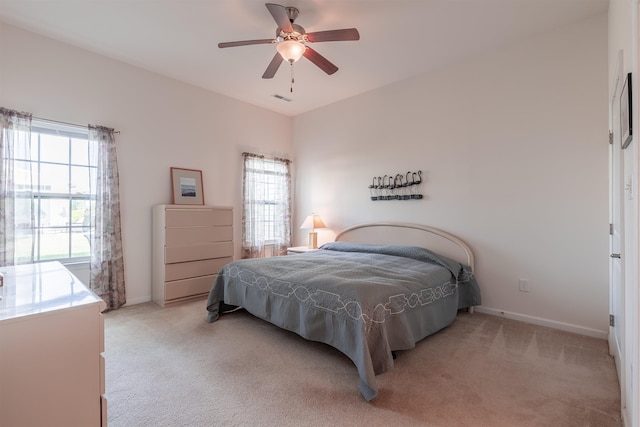 bedroom with multiple windows, ceiling fan, and light carpet