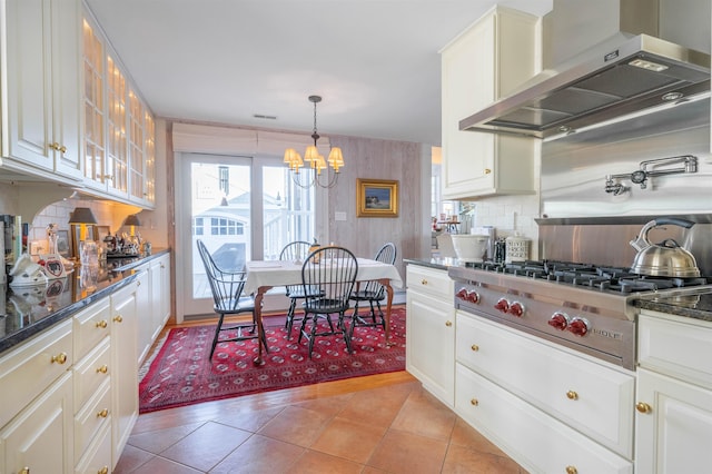 kitchen featuring decorative backsplash, stainless steel gas cooktop, wall chimney range hood, a notable chandelier, and white cabinets