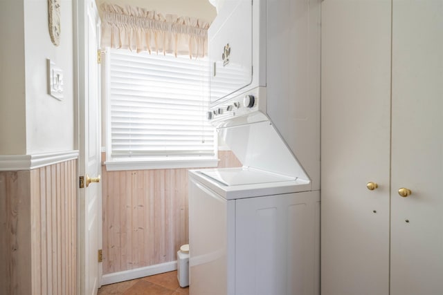 laundry area with wooden walls, light tile patterned flooring, and stacked washing maching and dryer