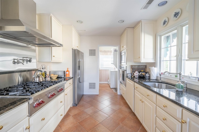 kitchen featuring stainless steel appliances, sink, dark stone counters, and wall chimney range hood