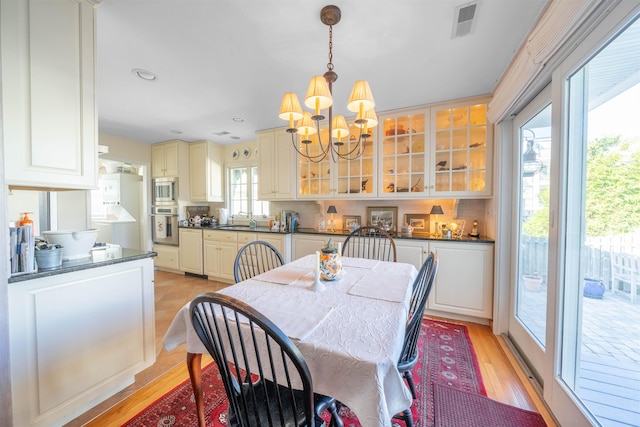 dining area with light hardwood / wood-style floors, a wealth of natural light, and a notable chandelier