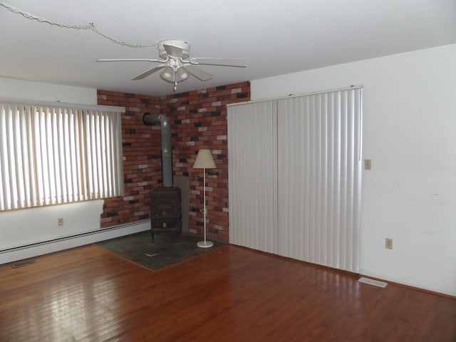 unfurnished living room with baseboard heating, a wood stove, a ceiling fan, and wood finished floors