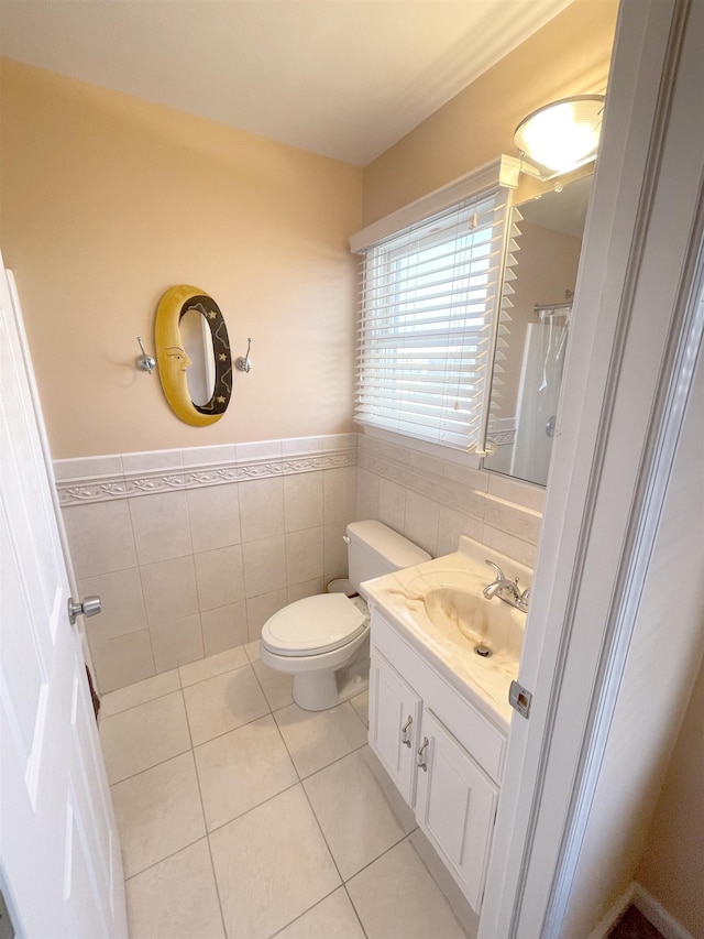 bathroom featuring a wainscoted wall, tile patterned floors, toilet, vanity, and tile walls