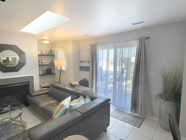 living area featuring a fireplace, visible vents, tile patterned floors, and a skylight