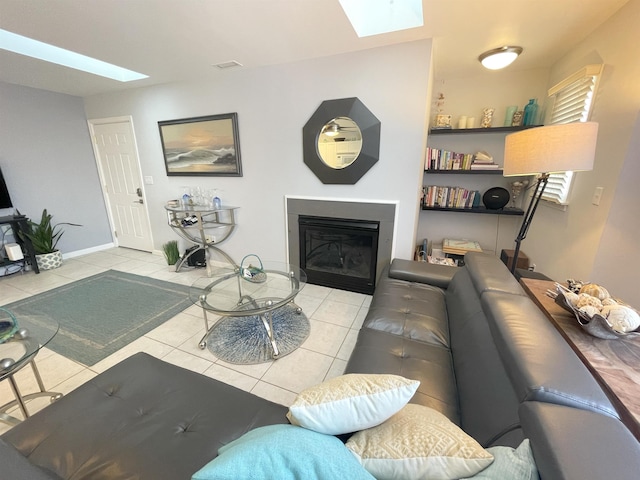 tiled living area featuring baseboards, a skylight, and a glass covered fireplace