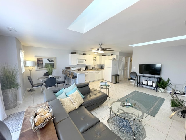 living area featuring baseboards, a skylight, ceiling fan, and light tile patterned floors