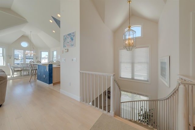 corridor featuring plenty of natural light, high vaulted ceiling, a notable chandelier, and light wood-type flooring