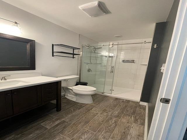 bathroom featuring a shower with door, vanity, and toilet