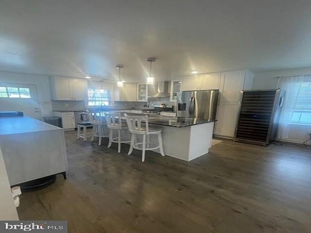 kitchen with white cabinetry, a center island, wall chimney exhaust hood, stainless steel appliances, and decorative light fixtures