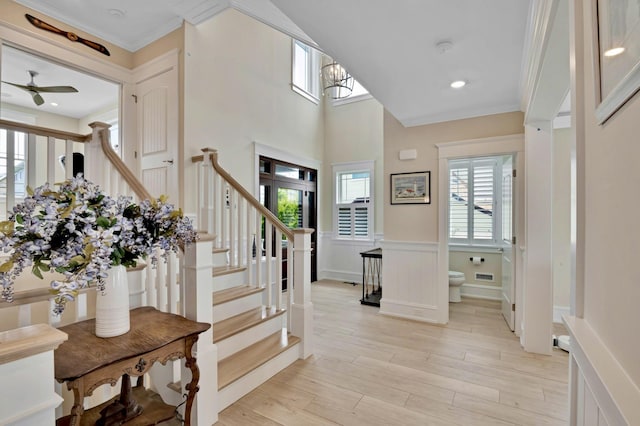 foyer featuring ornamental molding, a towering ceiling, ceiling fan, and light hardwood / wood-style floors