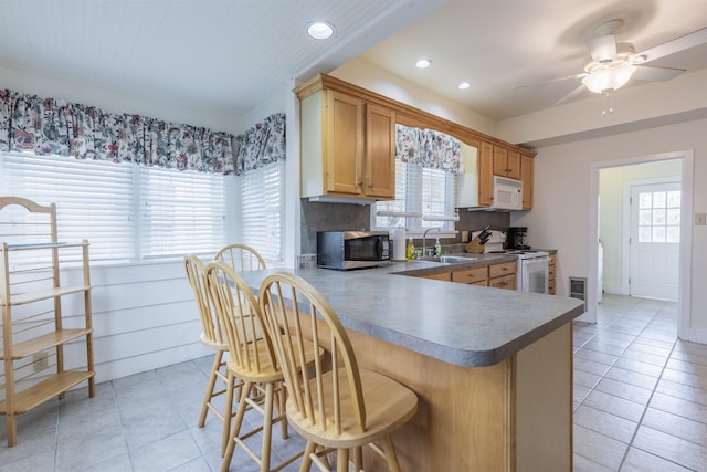 kitchen with kitchen peninsula, a kitchen breakfast bar, white appliances, ceiling fan, and sink