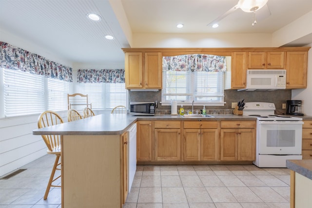 kitchen with sink, white appliances, a kitchen bar, decorative backsplash, and light tile patterned flooring