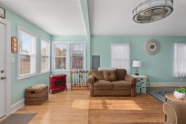 living room featuring beamed ceiling, wood-type flooring, a wood stove, and electric panel