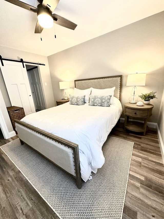 bedroom featuring a barn door, baseboards, wood finished floors, and a ceiling fan