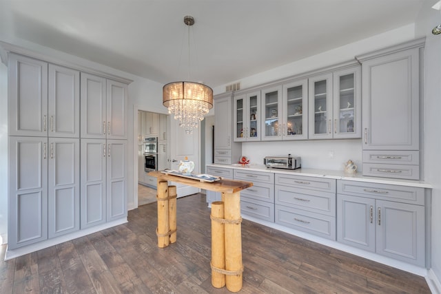 kitchen featuring dark wood finished floors, an inviting chandelier, glass insert cabinets, gray cabinetry, and light countertops