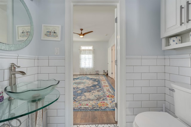 half bathroom with tile walls, toilet, wood finished floors, and wainscoting
