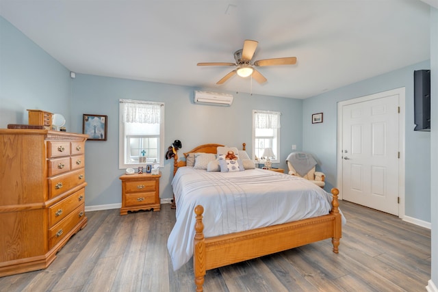 bedroom with a wall mounted air conditioner, wood finished floors, baseboards, and multiple windows