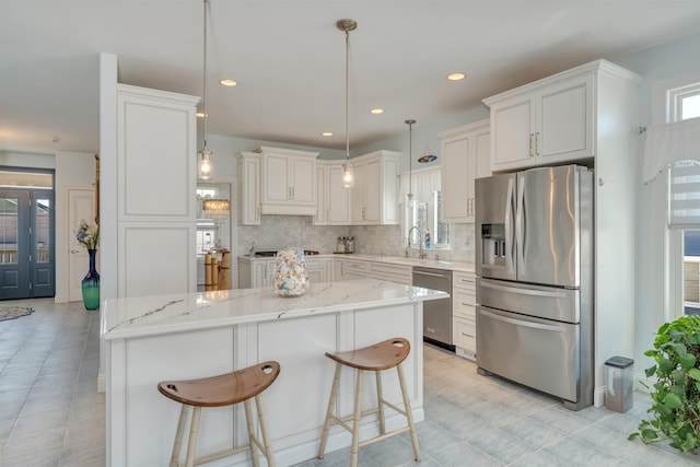 kitchen featuring a sink, light stone countertops, a center island, decorative backsplash, and appliances with stainless steel finishes