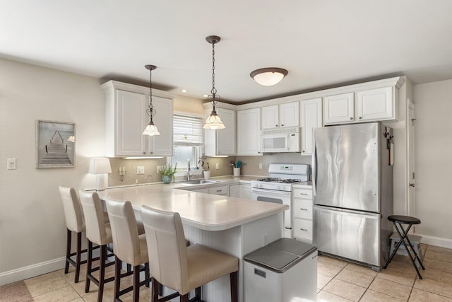 kitchen with white cabinets, a sink, white appliances, a peninsula, and a kitchen breakfast bar