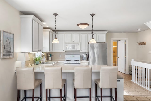 kitchen with light tile patterned floors, a peninsula, white appliances, a sink, and light countertops