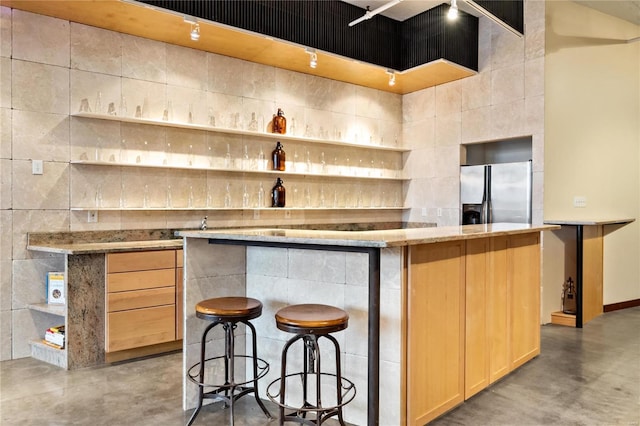 kitchen featuring a high ceiling, a breakfast bar area, light brown cabinetry, and stainless steel fridge