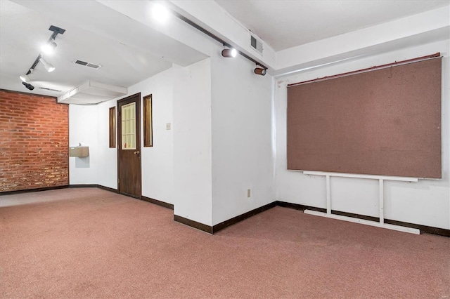 carpeted spare room with rail lighting and brick wall