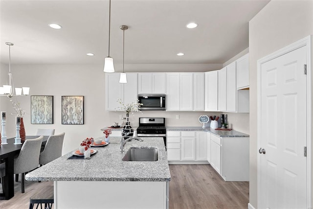 kitchen with pendant lighting, light wood-type flooring, stainless steel appliances, sink, and white cabinetry